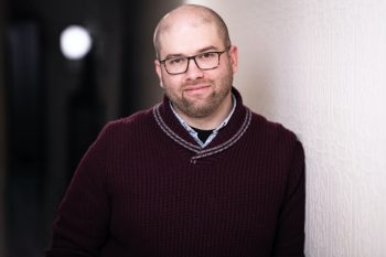 image of Ian Garrett wearing a burgundy sweater and glasses. slightly unshaved
