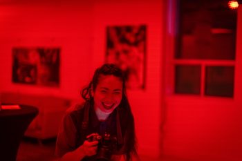 image of Rachel Wang laughing in a room with posters on the wall, entire image is washed in red